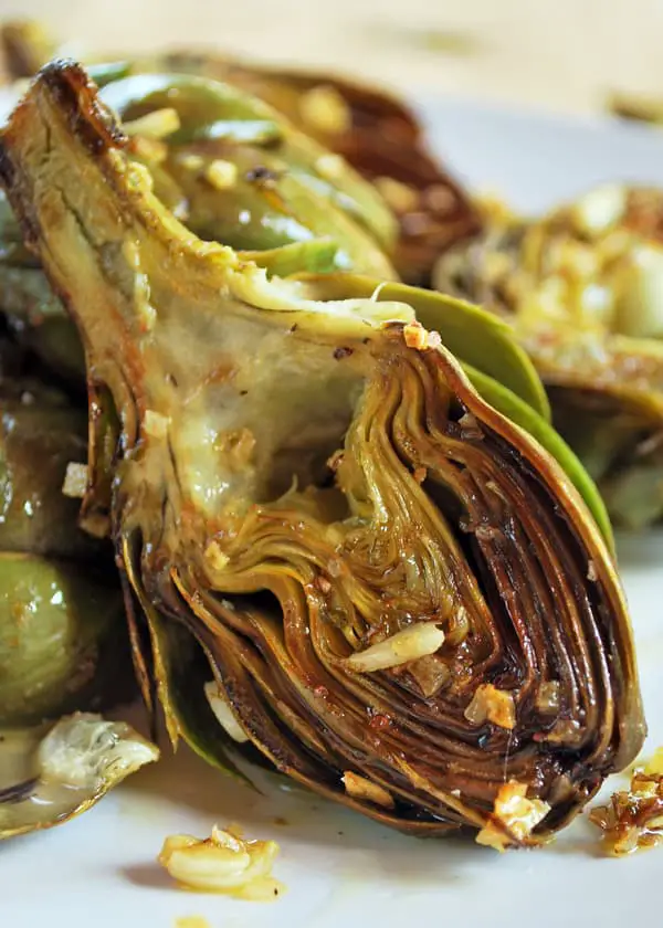 Alcachofas asadas cortadas por la mitad, servidas en un plato. 