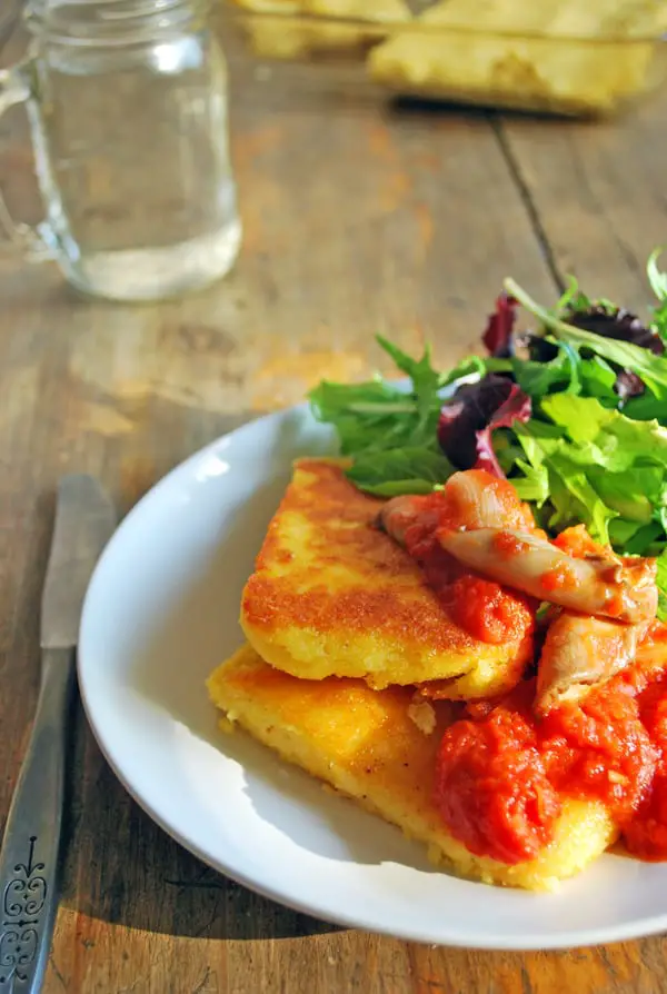 Polenta crujinete por fuera, suave por dentro con una espectacular salsa de jitomate y setas. La polenta es un plato de origen italiano que se hace a partir del maíz y es perfecta para cuando hace frío pero al hacerla de esta manera no importa si hace frío o calor siempre se me antoja. Para hacer este plato lo primero que hay que hacer es un caldo de verduras. En una cacerola sofreímos un poco de cebolla, pimiento, ajo, zanahoria y apio, en cuanto tomaron un poco de color llenamos la olla con agua y lo llevamos al hervor por lo menos por media hora. Este caldo será la base para cocinar la polenta y le dará un sabor único, si prefieren hacerlo con agua se puede sin problema y también será rica pero un buen caldo definitivamente le da mucha más profundidad de sabores al plato. Una vez que tienen el caldo deben cocinar la polenta (como diga la caja) poniendo poco a poco la polenta para que no se hagan grumos y revolviendo constantemente. Cuando esta lista la es momento sazonarla bien, agregarle una buena cantidad de queso parmesano y gouda, un poco de mantequilla y si quieren alguna hierba de olor. El resultado será una textura sedosa. Una vez lista en una bandeja previamente aceitada colocamos la polenta, la estiramos dejándola a un grosor de un centímetro más o menos y los dejamos enfriar por completo. Verán que al enfriarse se endurece y es entonces momento cortarla en porciones para dorarlas. Por otro lado, hay que hacer una salsa la cual puede ser una como la de esta pasta, o un ragú, pero esta vez hice una con setas la cual quedo de lujo con la polenta. Para eso cocine pimiento morrón, cebolla y ajo con un poco de mantequilla hasta que las verduras estaban suaves, le puse las setas y una vez que soltaron sus jugos les agregue el jitomate licuado. La cocine por unos 20 minutos, la saque del fuego y le puse bastantes hojas de albahaca fresca. Lo siguiente es armar el plato, para eso en una sartén bien caliente con un poco de aceite doramos los trozos de polenta por ambos lados, una vez crujientes los ponemos en un plato y por encima ponemos un poco de la salsa. Es una delicia que no se pueden perder.