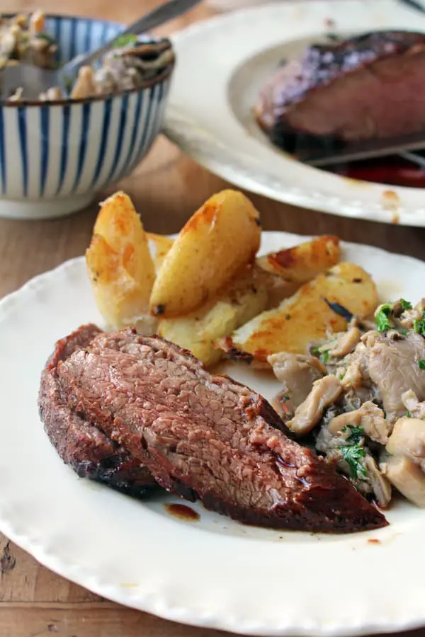 Un plato con un trozo de carne al horno, unas papas y unas setas. 