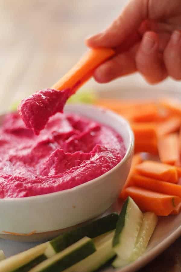 hummus de betabel servido en plato hondo acompañado de zanahorias, pepinos y apio.