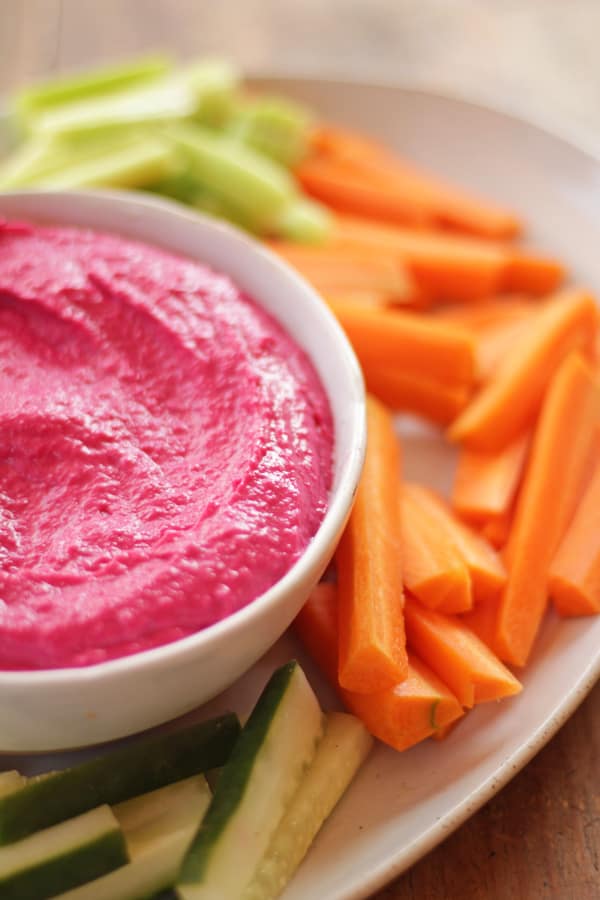 hummus de betabel servido en plato hondo acompañado de zanahorias, pepinos y apio.