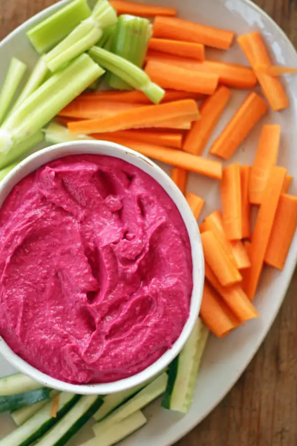 hummus de betabel servido en plato hondo acompañado de zanahorias, pepinos y apio.