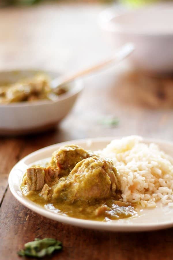 Pierna de cerdo en salsa verde servida en un plato junto a un poco de arroz blanco. 