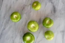 6 tomates verdes pelados y limpios sobre una mesada de mármol