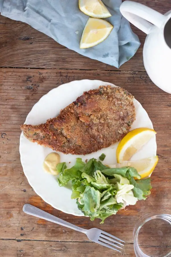 Milanesa servida en un plato con limón y ensalada.