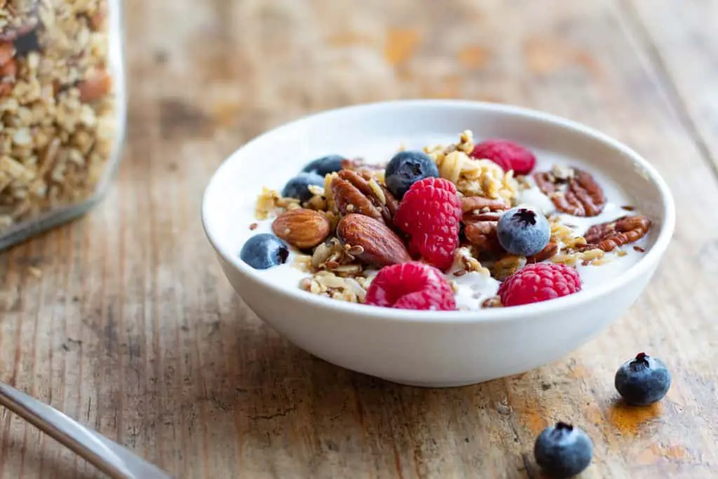 Plato hondo servido con yogurt, granola, frambuesas y blueberry