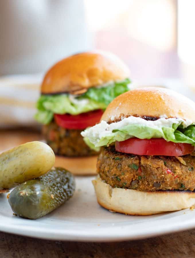 Hamburguesa de lentejas servidas con jitomate, lechuga y unos pepinillos.