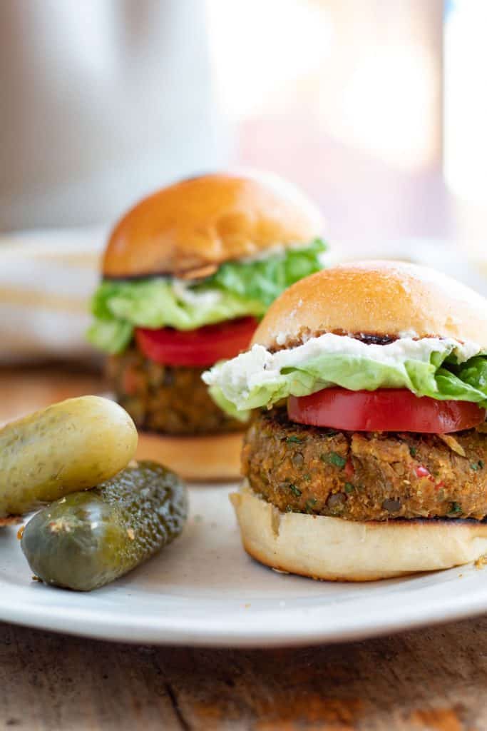 Hamburguesa de lentejas servidas con jitomate, lechuga y unos pepinillos.