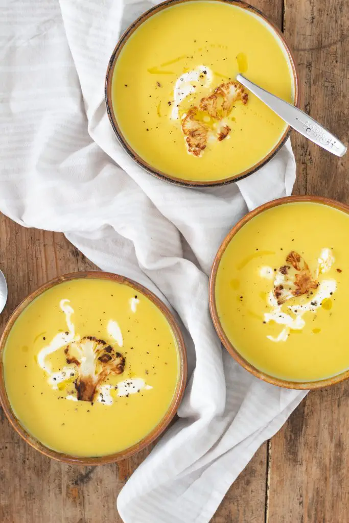 crema de colififlor dorada servida en tres platos hondos junto a una servilleta de tela