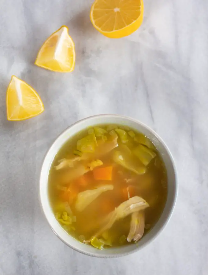 caldo de pollo con verduras servido en un tazon hondo, junto a unos limones cortados.