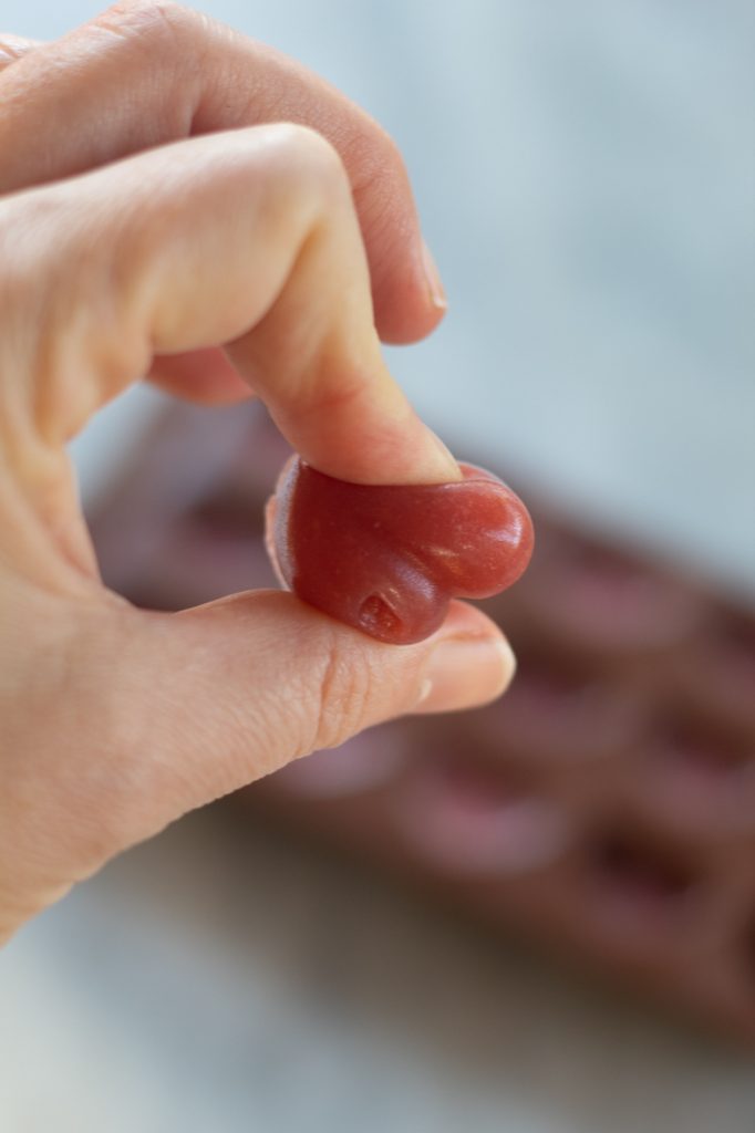 mano aplastando una gomita de fresa en forma de coarzón