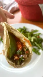 Una mano tomando un taco de tinga de pollo con aguacate y frijoles