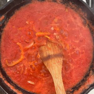 cebollas y pimientos cocinandose junto con jitomate molido en una olla de hierro