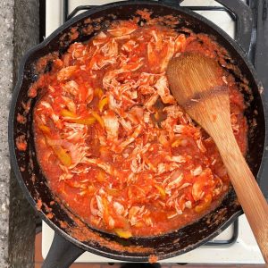 Cocinando pollo en salsa de jitomate en una sarten de hierro