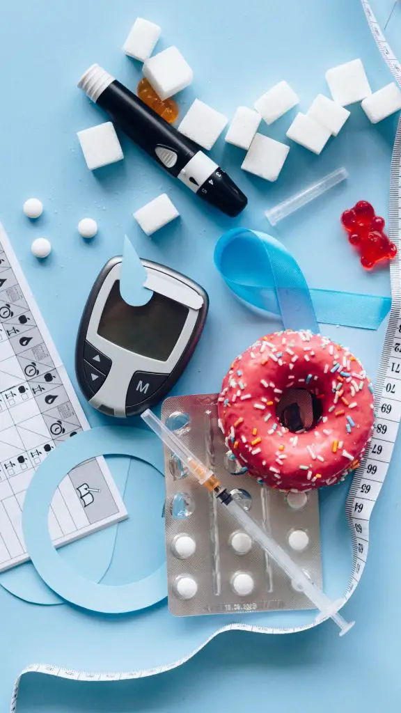 Cubitos de azúcar, glucómetro, una dona, insulina en una jeringa, pastillas para la diabetes. 